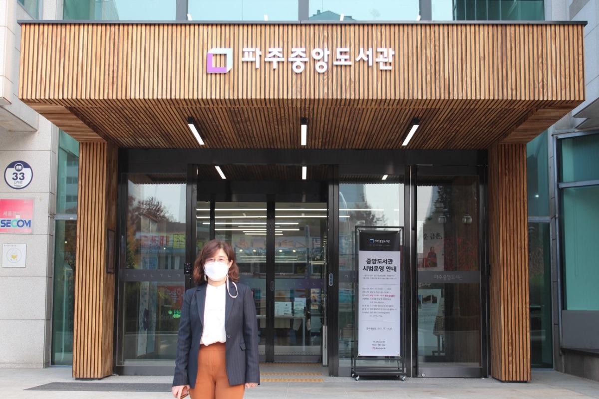 파주시중앙도서관 정문에 선 윤명희 관장. 뒤로 도서관 로고가 보인다.