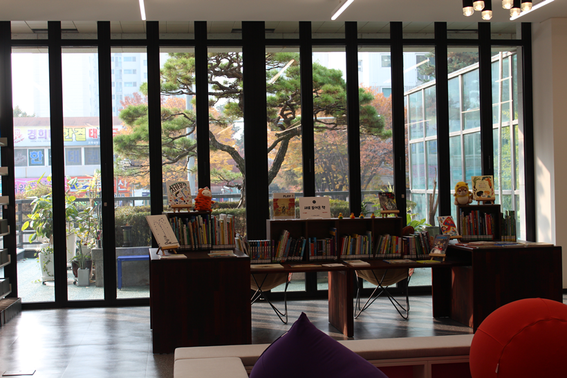 1층 새로 들어온 책 코너_창밖으로 개관 기념식수 소나무가 보인다.